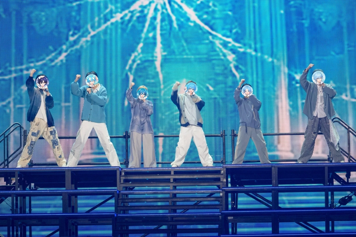 青い背景のステージで、アニメキャラクターの顔を持つ6人組がパフォーマンス