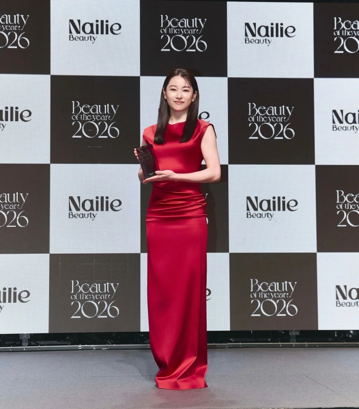 赤いロングドレスを着用した女性が、Nailie BeautyとBeauty of the year 2026と書かれた背景の前でトロフィーを持ち、笑顔で立っている授賞式の様子です。
