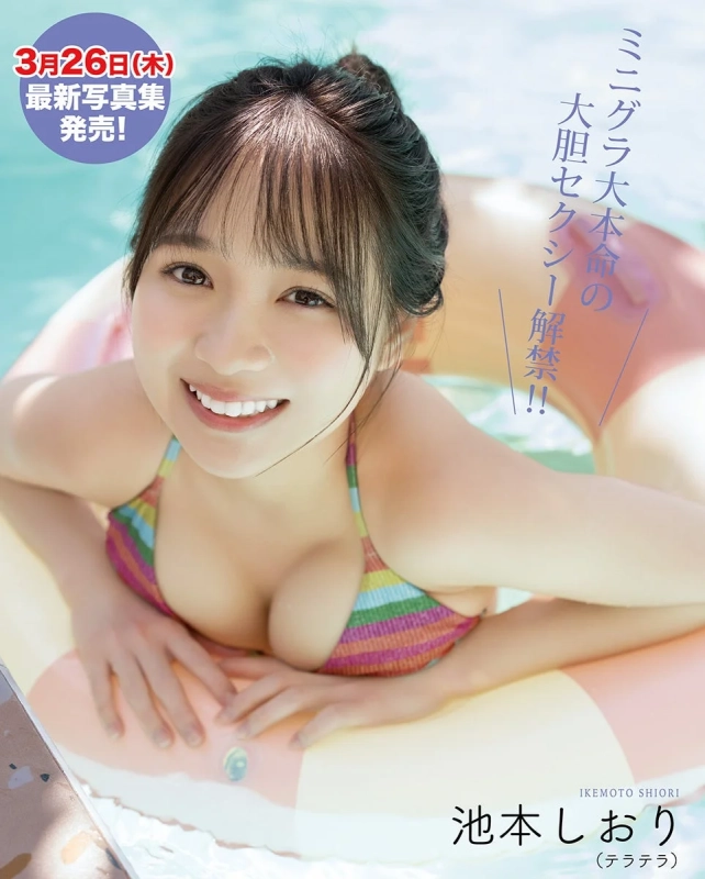 水色のプールで浮き輪に乗り、笑顔を見せる女性「池本しおり」のグラビア画像です。カラフルなストライプのビキニを着用しており、3月26日に最新写真集が発売されることを告知しています。