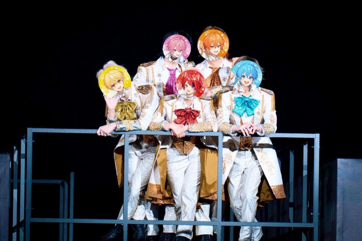 豪華な白と金の衣装を身につけた5人組のアイドルグループがステージ上でポーズ