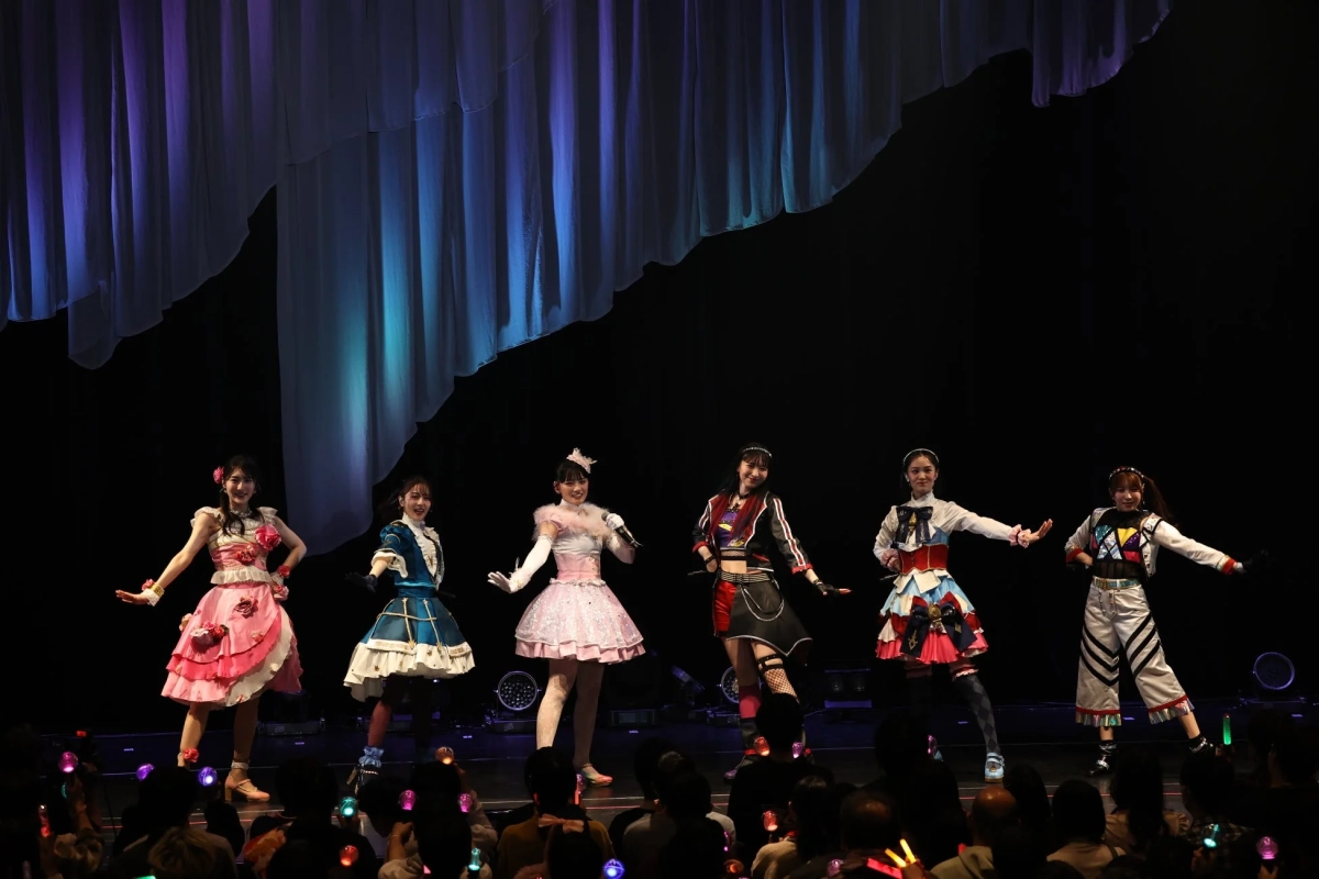 カラフルな衣装を着た6人の女性アイドルグループがステージでパフォーマンス