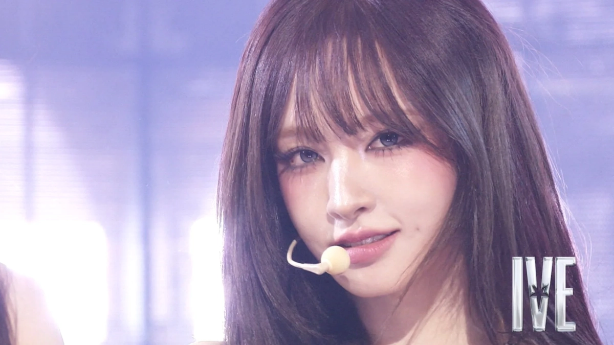 長いダークヘアの女性がヘッドセットマイクを装着し、紫色の照明の中でパフォーマンス