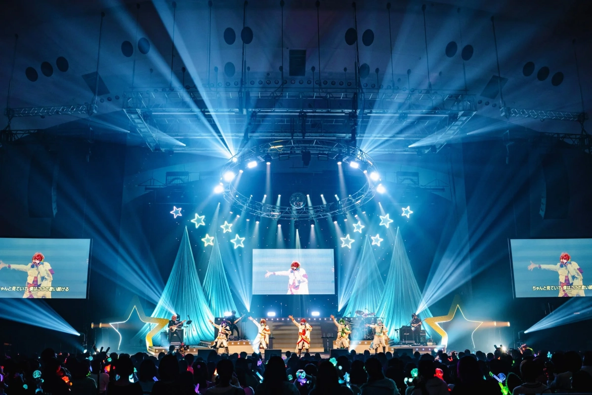 青い照明のステージでパフォーマンスしている画像