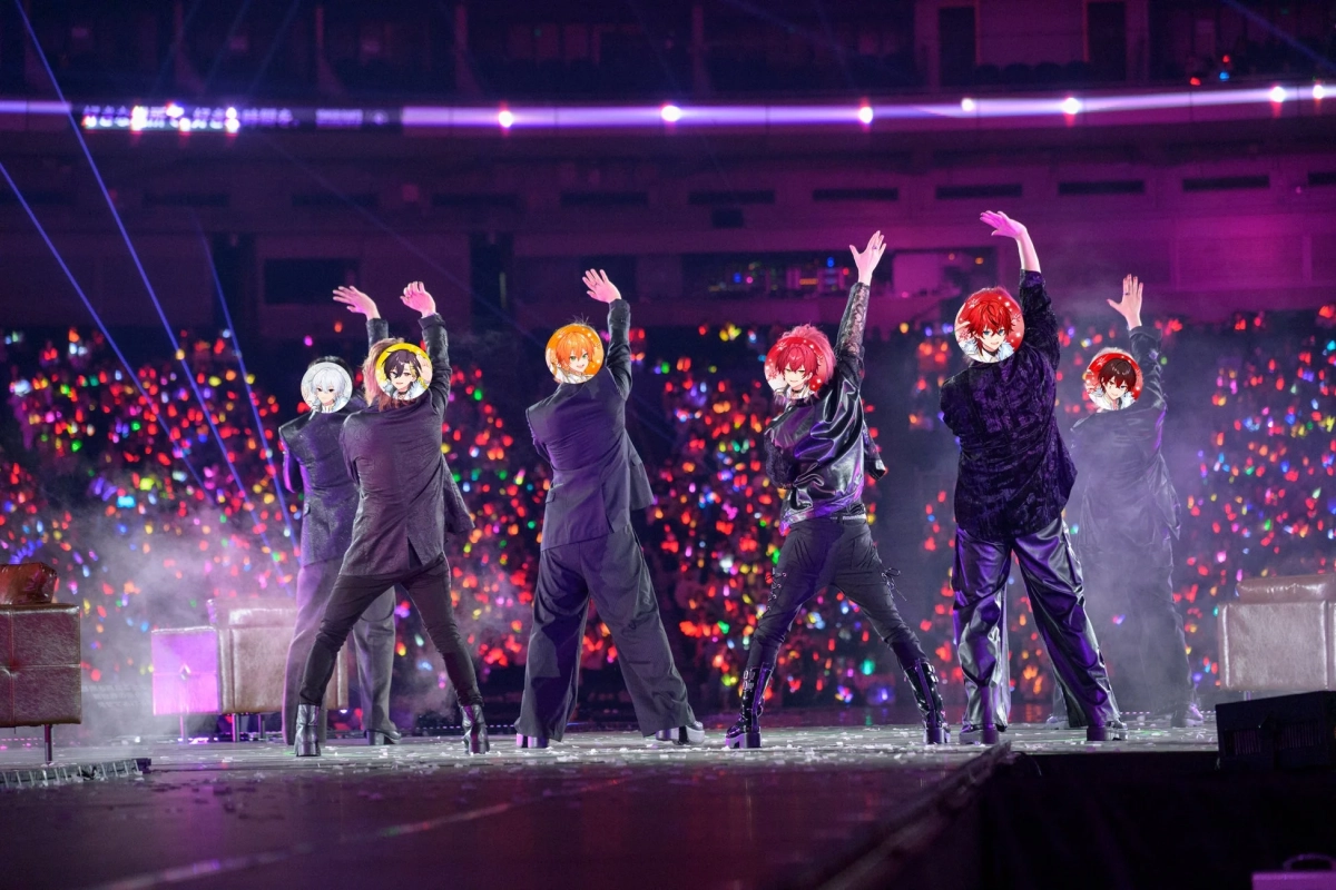 アニメキャラクターの顔が合成された6人組が、ペンライトで埋め尽くされた大勢の観客を背に、ステージでパフォーマンス