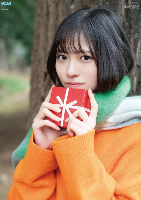 日向坂46の正源司陽子が、オレンジ色のセーターとマフラーを身につけ、赤いプレゼントの箱を抱えているポートレート。冬の屋外でカメラを見つめる彼女の姿が印象的です。
