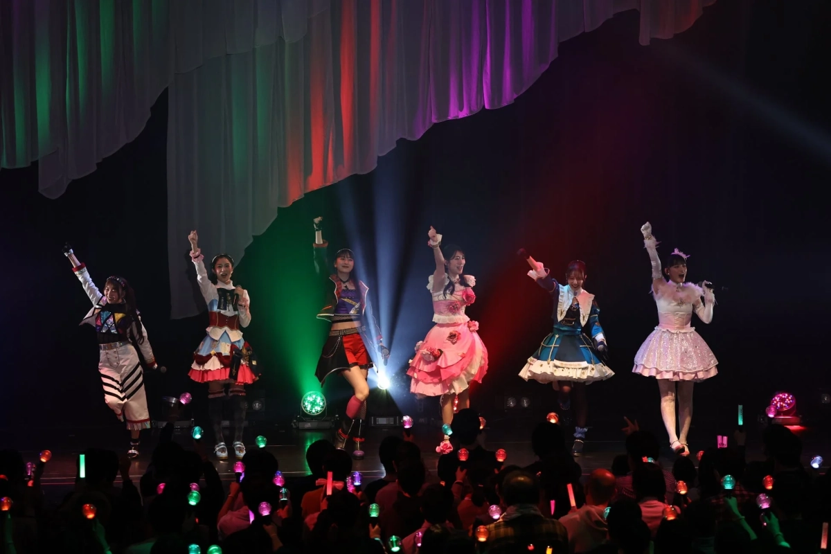 カラフルな衣装をまとった6人の女性アイドルグループがステージでパフォーマンス