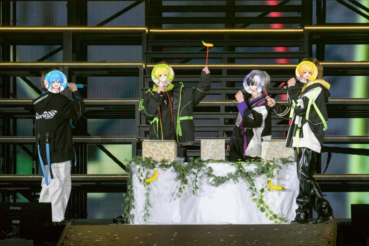 ステージ上で4人のパフォーマーがマイクを持ち、歌唱またはイベントを行っている様子