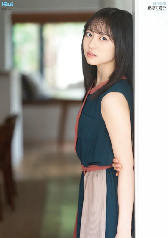 日向坂46の正源司陽子が屋内でカメラを見つめているポートレート。緑とベージュのワンピースを着用し、清楚で落ち着いた雰囲気を醸し出している。自然光が入り込む空間で、彼女の魅力が引き立つ一枚です。