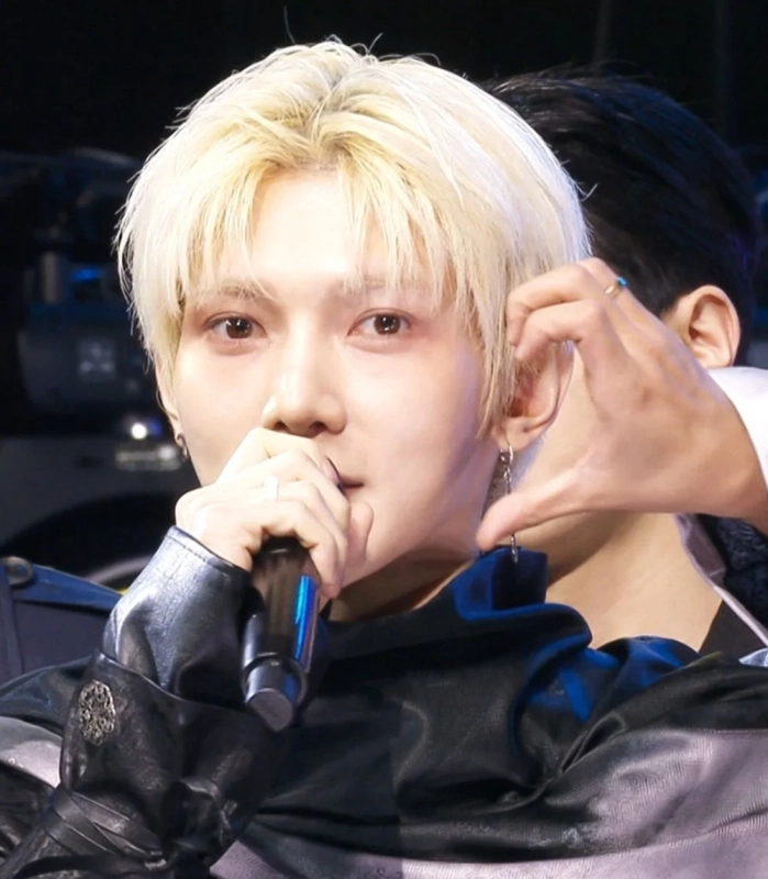 金髪の男性アイドルがマイクを握り、ステージ上でハートポーズ