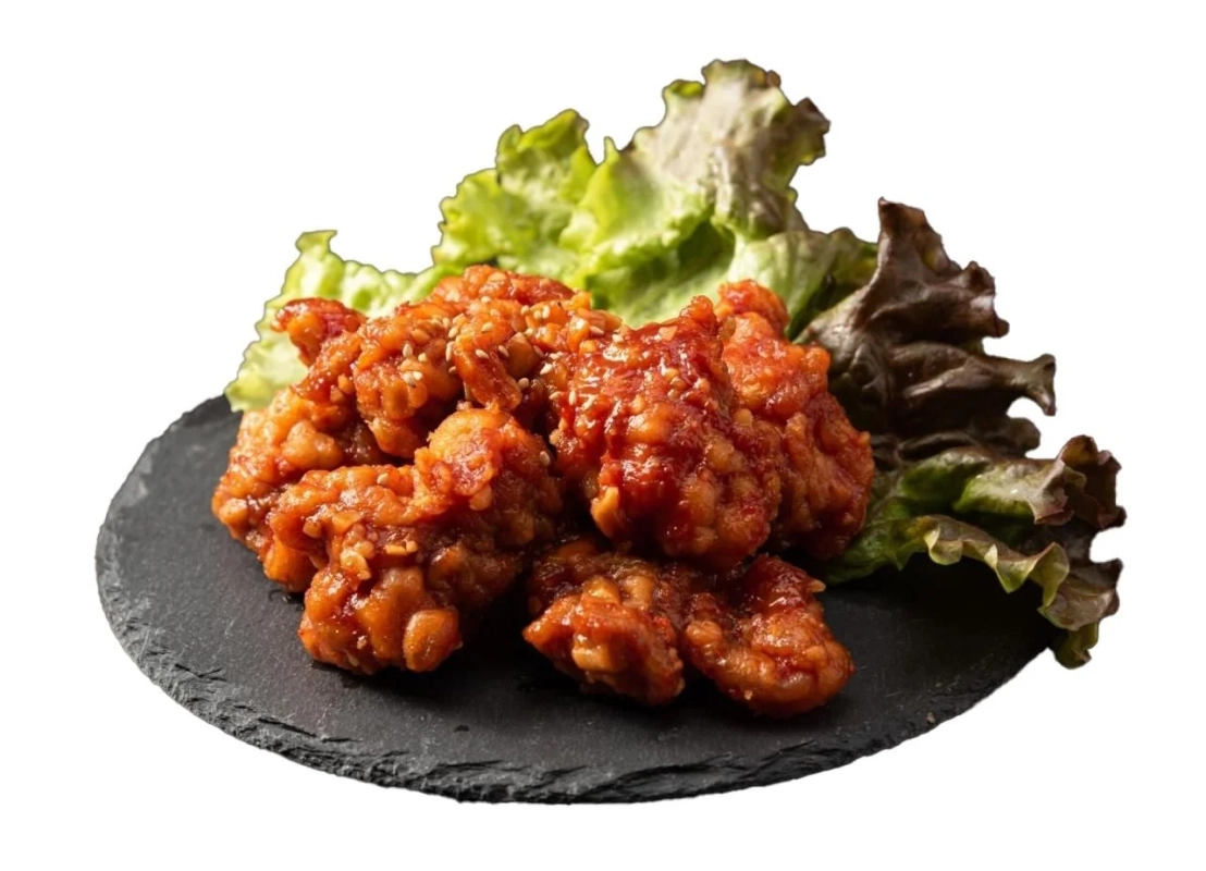 甘辛いタレで絡めた揚げ鶏肉が、白いごまとレタスと共に黒いプレートに盛り付けられています