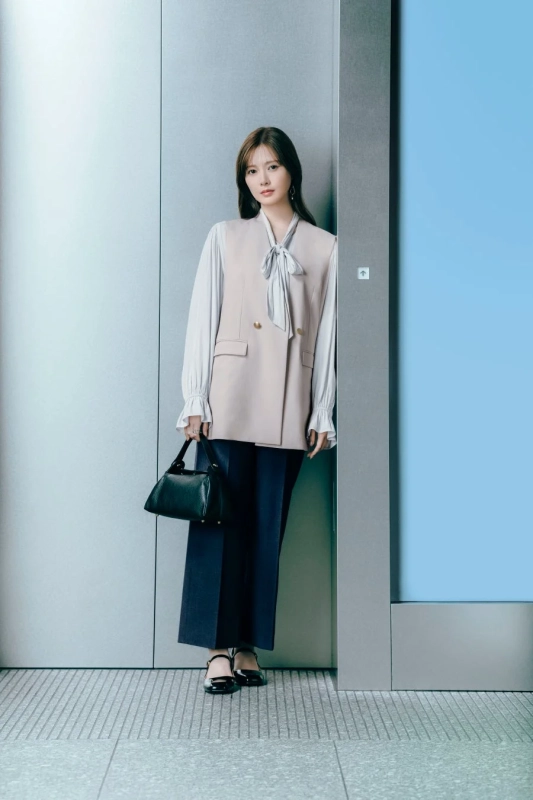 ベージュのベストと白のブラウス、ダークカラーのパンツを着用した女性