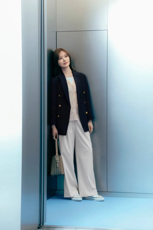 ネイビーのブレザー、ピンクのカーディガン、オフホワイトのワイドパンツを着用した女性