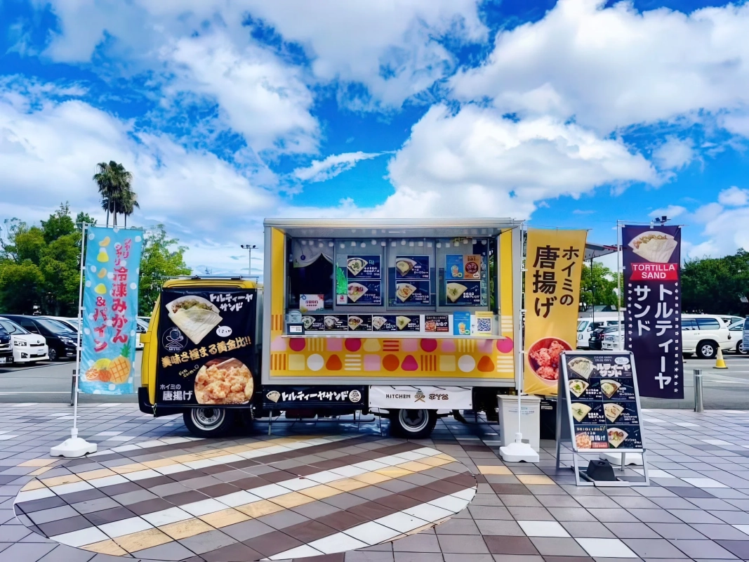 快晴の空の下、カラフルなフードトラック「KITCHEN Hoimi's」が営業している様子