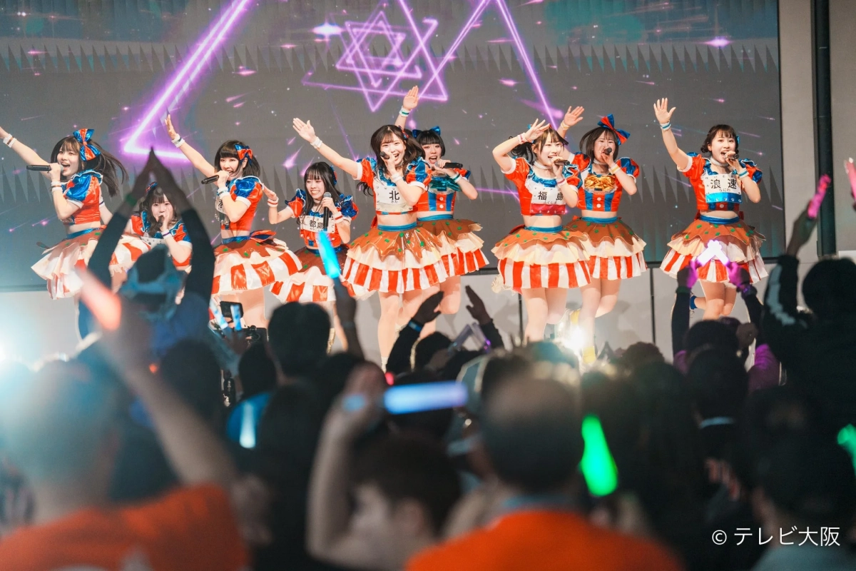 カラフルな衣装をまとったアイドルがステージでパフォーマンスする様子