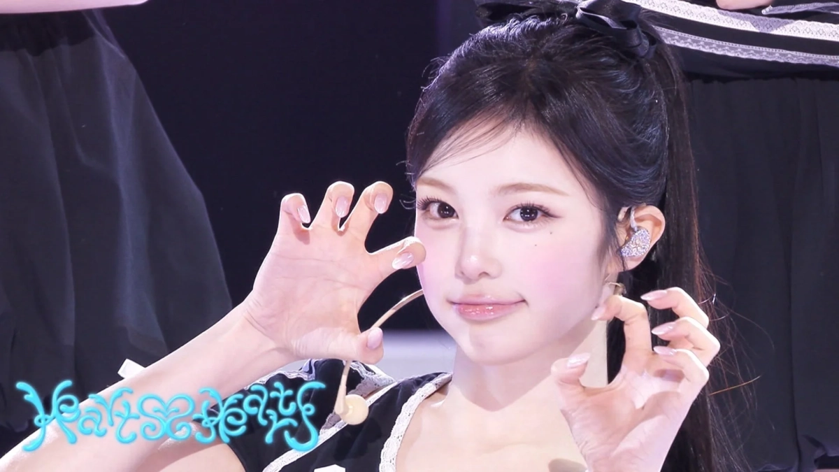 ステージ上で猫のようなポーズをとる若い女性のアイドルが写っています。彼女は黒い衣装を身につけ、ポニーテールにした長い髪とイヤモニが特徴的です。背景は暗く、照明が当たっています。