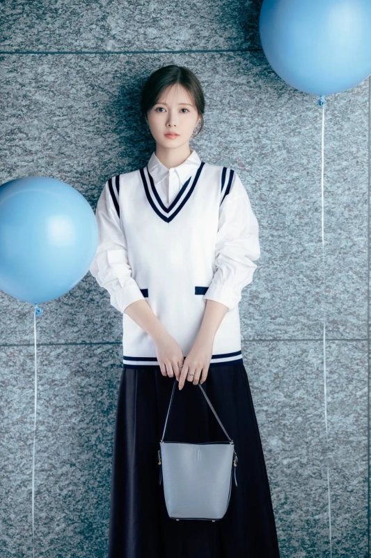 白いシャツとネイビーのストライプが入ったベスト、黒いロングスカートを着用した女性