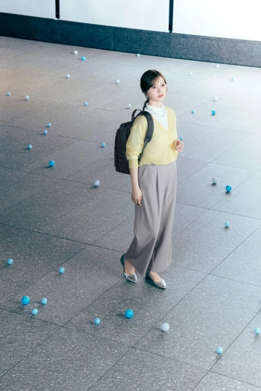 黄色のカーディガンとグレーのパンツを着用し、リュックを背負った若い女性