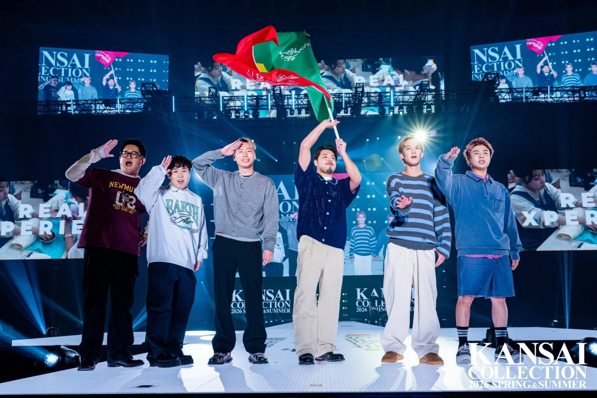 ファッションショーのステージで、6人の男性がポーズを取り観客に挨拶しています