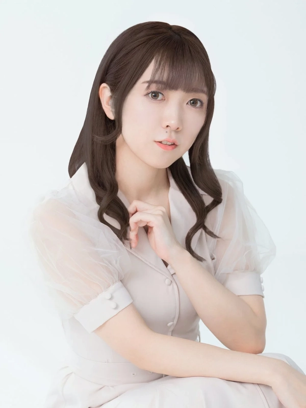 白い背景の前で、ベージュのブラウスを着用したロングヘアの若い女性が優雅なポーズをとっているポートレート写真