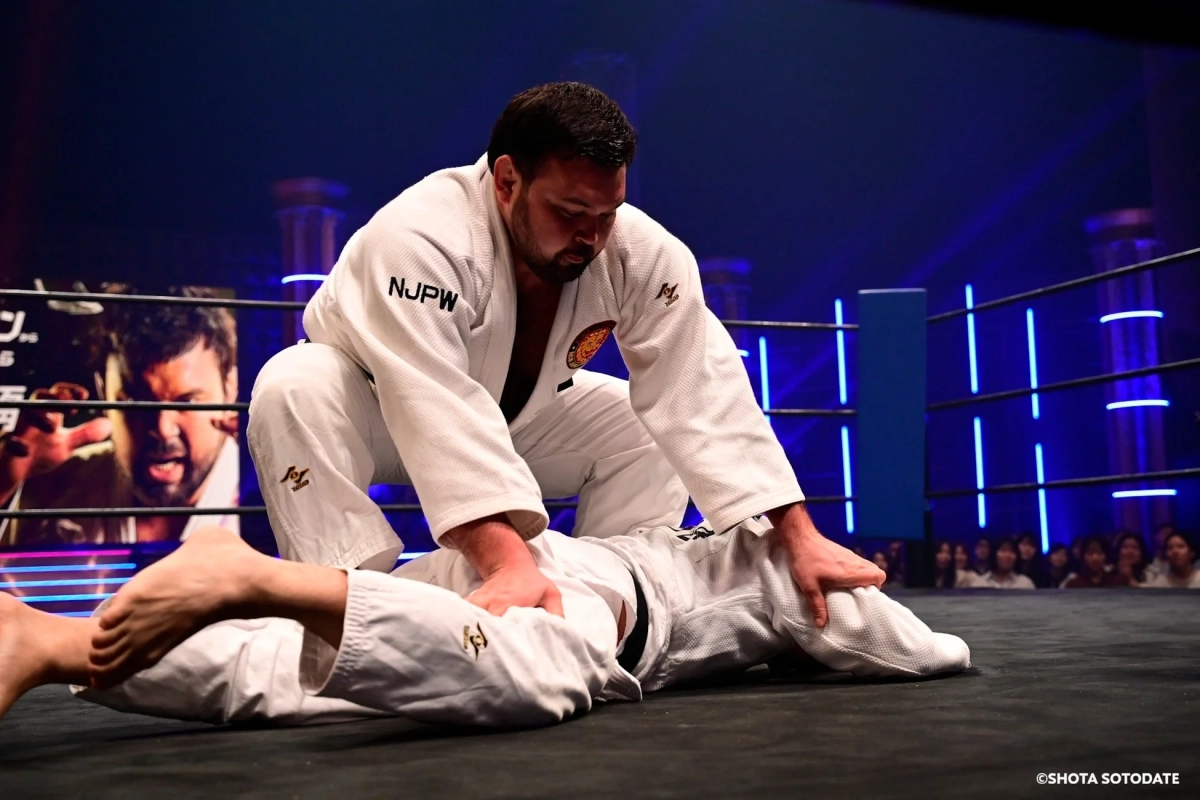 白い道着を着た二人の男性がリング上で寝技を繰り広げている格闘技の試合風景です。