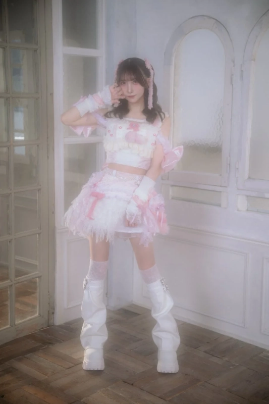 ピンクと白のフリルの衣装を着た若い女性が、窓のある室内でポーズをとっています。