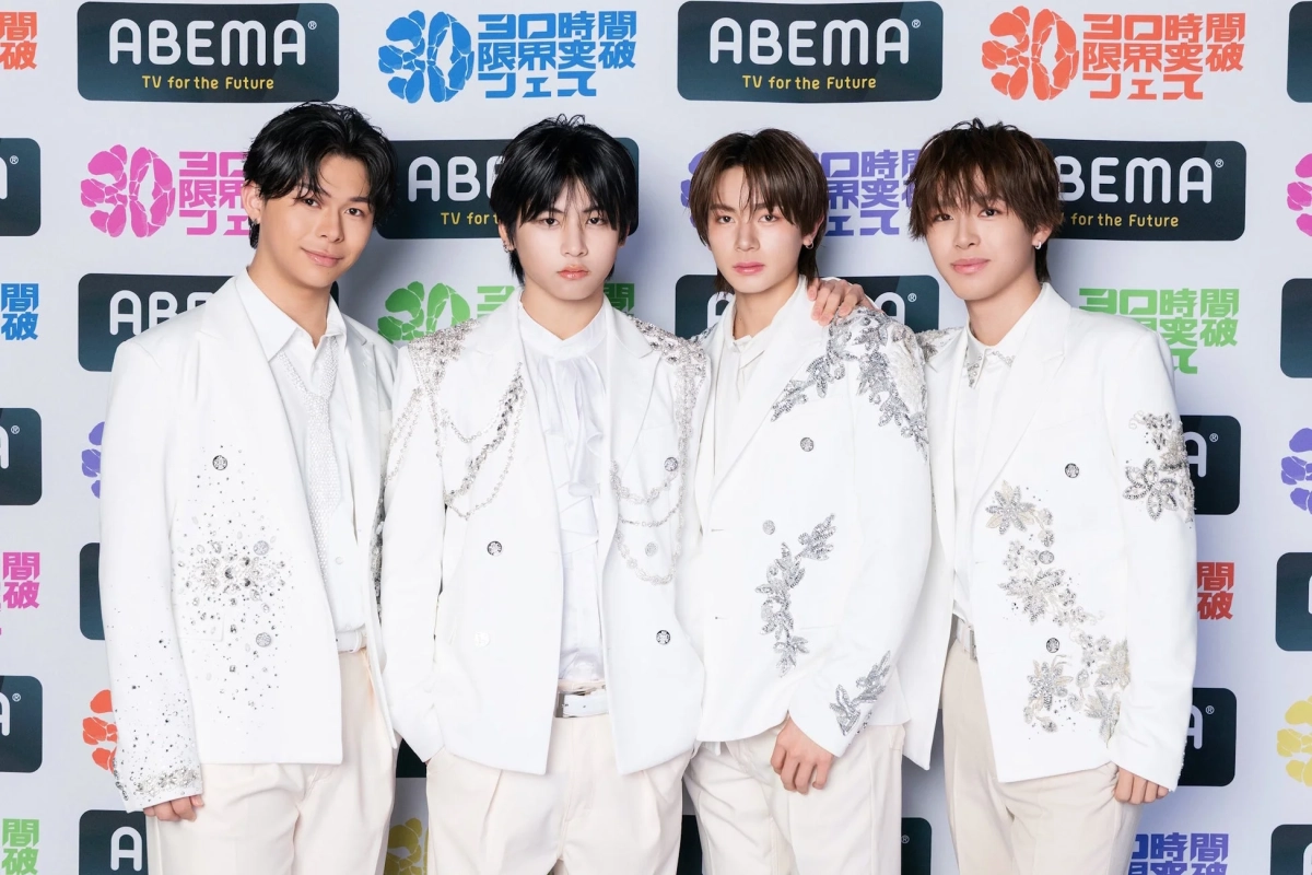 白を基調とした華やかな衣装をまとった4人組男性アイドルグループが、ABEMAのイベントロゴを背景にポーズをとっている集合写真です。