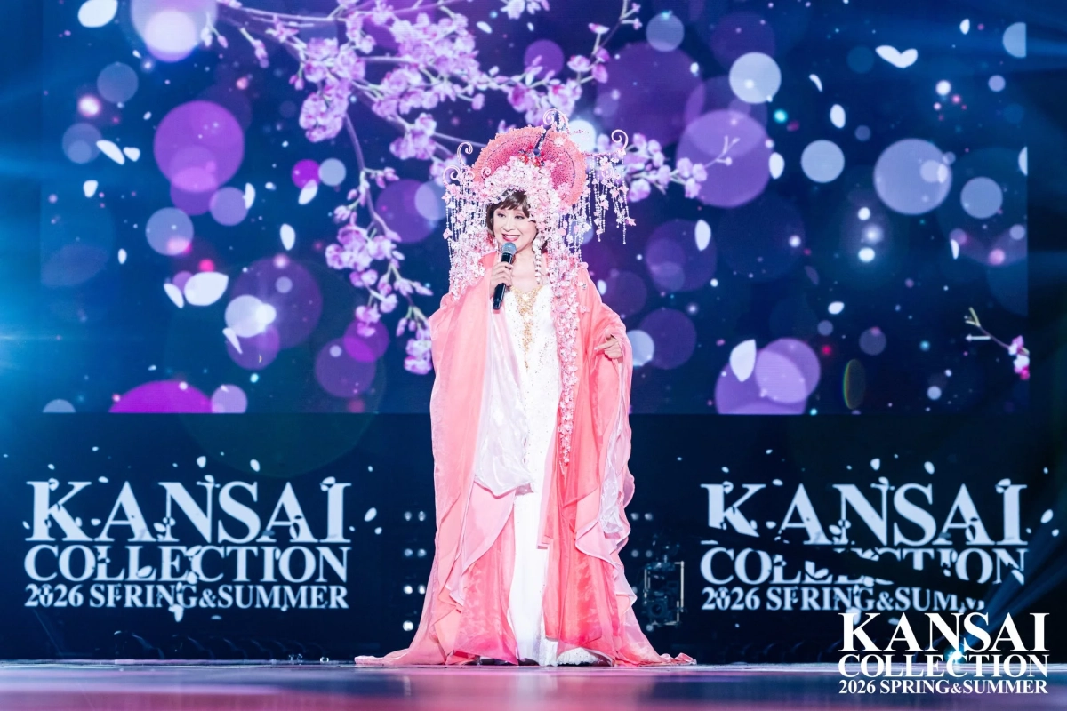 豪華なピンクの衣装と華やかなヘッドドレスを身につけた女性がマイクを持ち、ステージで歌っている