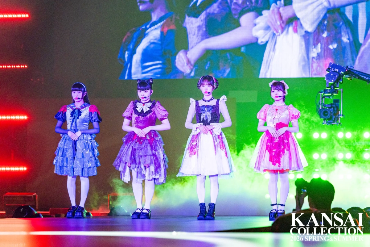 カラフルなフリルのドレスを着た4人の女性が、明るくライトアップされたステージに立っています