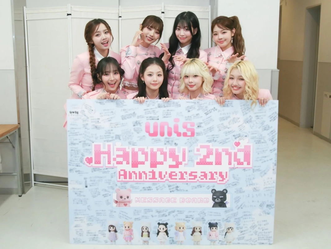 UNISメンバーが2周年を祝うメッセージボードを囲む様子
