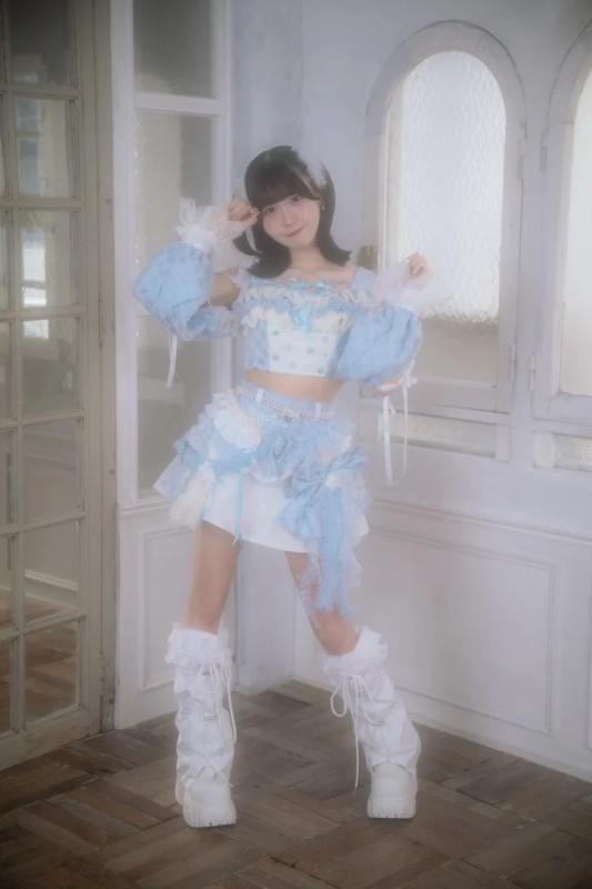 水色と白のフリルが可愛いツーピース衣装を着た若い女性が、明るいスタジオでポーズをとっています。