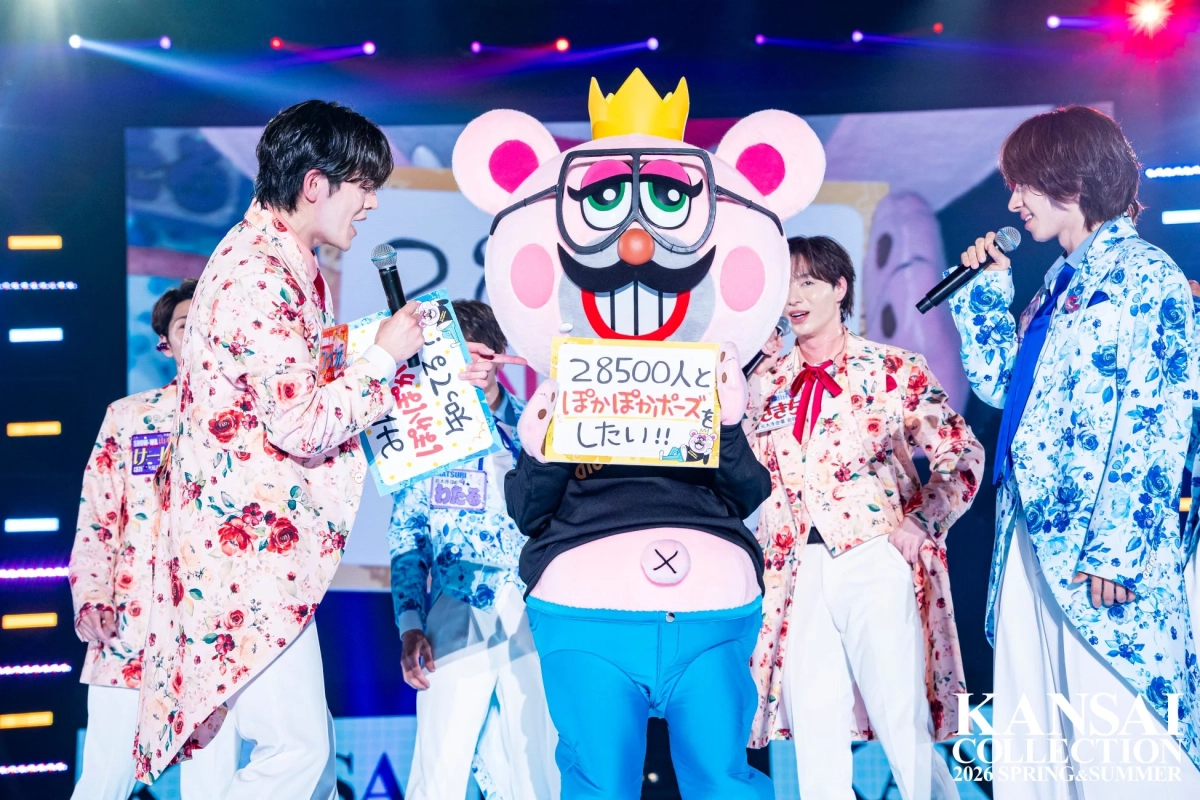 フローラル柄のスーツを着た男性パフォーマーたちが、ピンクのマスコットキャラクターと共に盛り上がっている様子