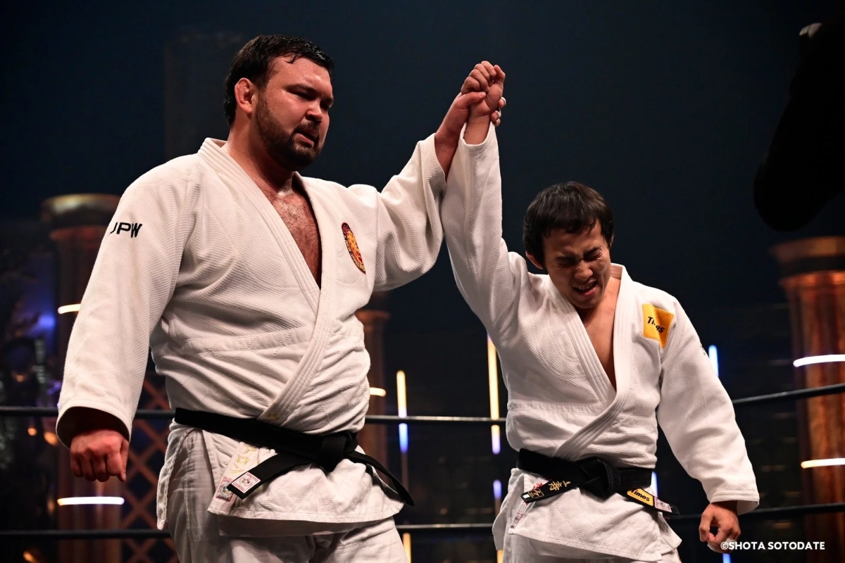 柔道着を着用した二人の男性がリング上で、片方がもう片方の腕を高く掲げている。