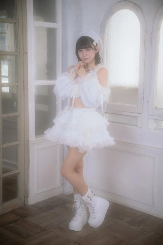白いフリルとレースの衣装を身につけた若い女性が、白い窓を背景にポーズをとっています。