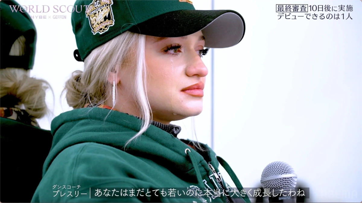 緑のパーカーと帽子をかぶった若い女性が涙を流している。タレントオーディションの感動的な瞬間を捉えた一枚。