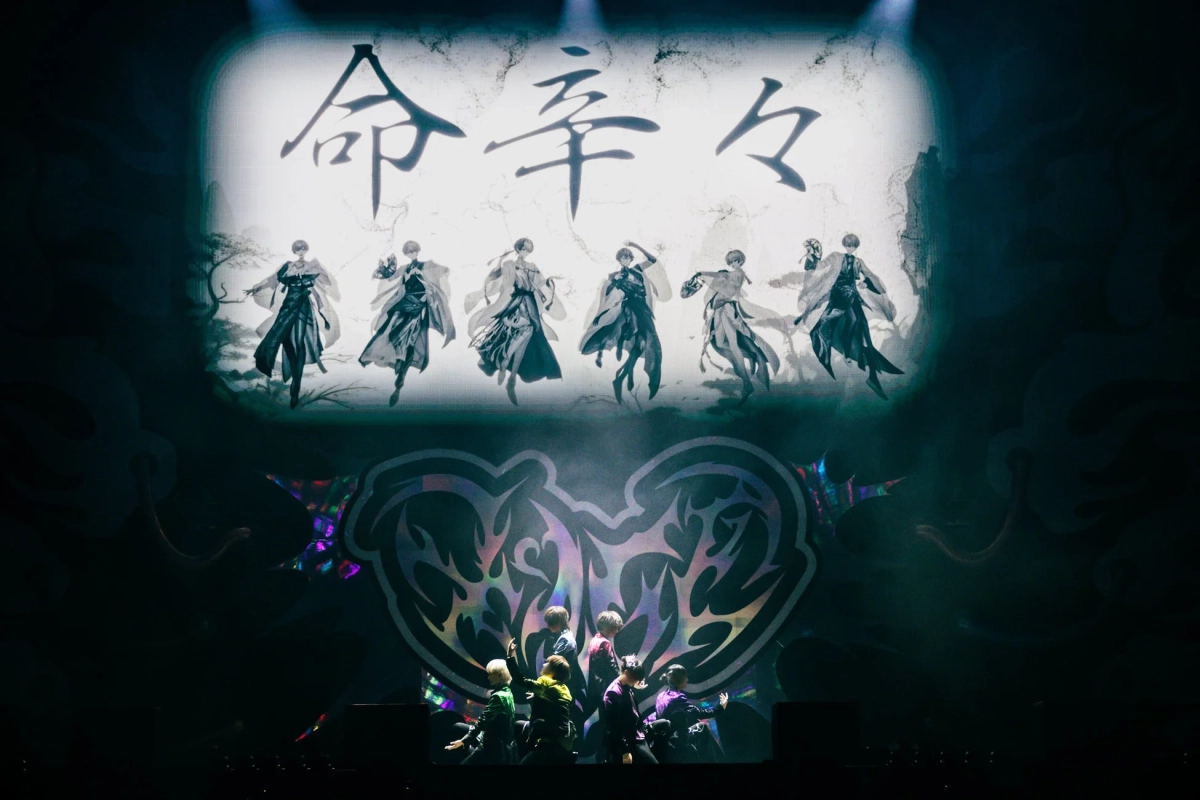 ステージ上で、上部に「命辛々」の文字とアニメ風の人物が映し出され、下部には実際のパフォーマーたちが立つライブパフォーマンスの様子