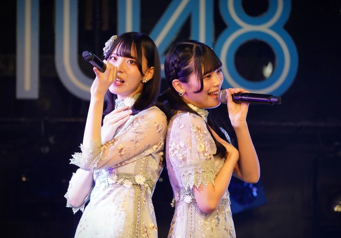 ライブステージで、マイクを手に歌う二人の女性アイドル