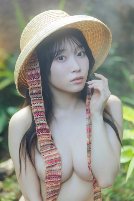 麦わら帽子を被った若い女性が、緑豊かな自然の中でカメラを見つめているポートレート