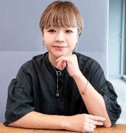ショートヘアの女性が黒いシャツを着てテーブルに座り、顎に手を当てているポートレート