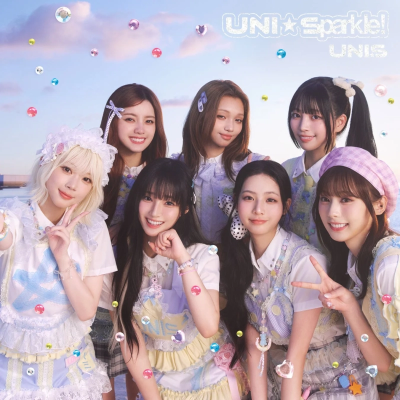 パステルカラーの可愛らしい衣装を身につけた7人の女性アイドルグループが、笑顔でポーズをとる集合写真