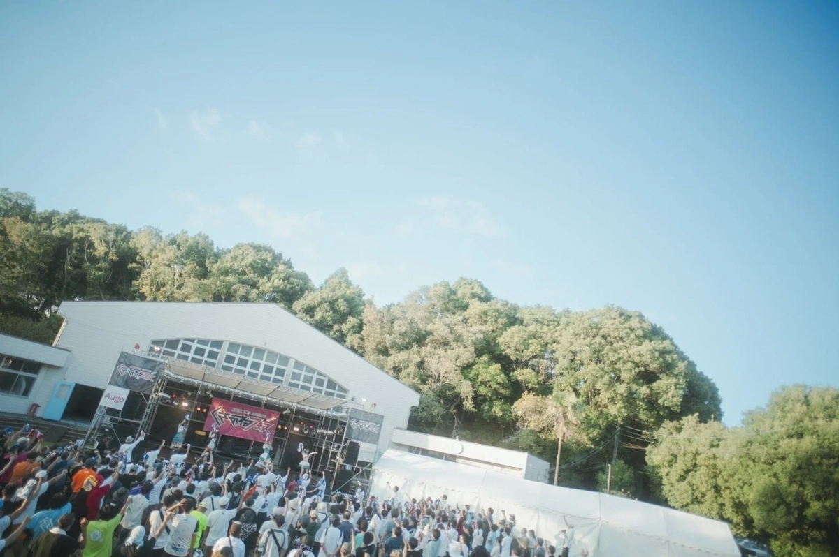 青い空の下、屋外ステージでライブパフォーマンスが行われています