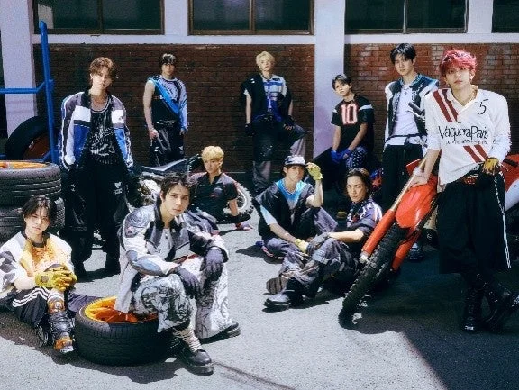 若い男性アイドルグループが、バイクやタイヤが置かれたストリート風の場所でポーズをとっている集合写真