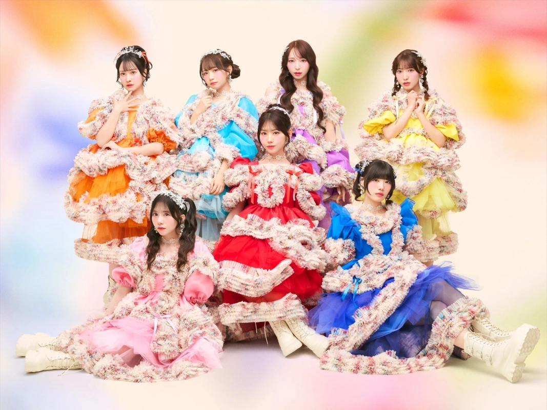 カラフルなフリルと花柄のドレスを身につけた7人の女性アイドルグループ