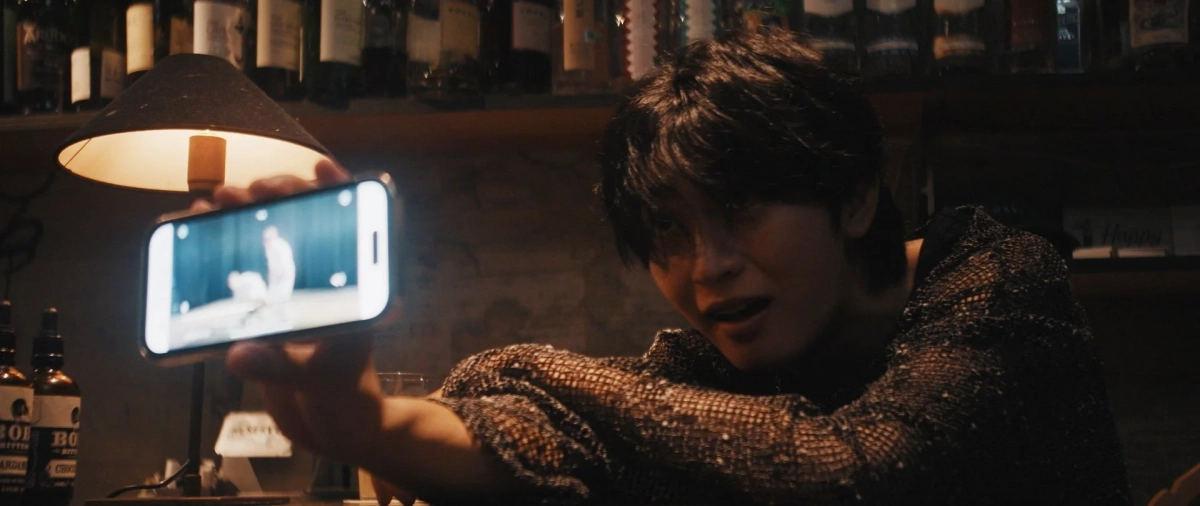映画のシーン：バーでスマホを見る男性