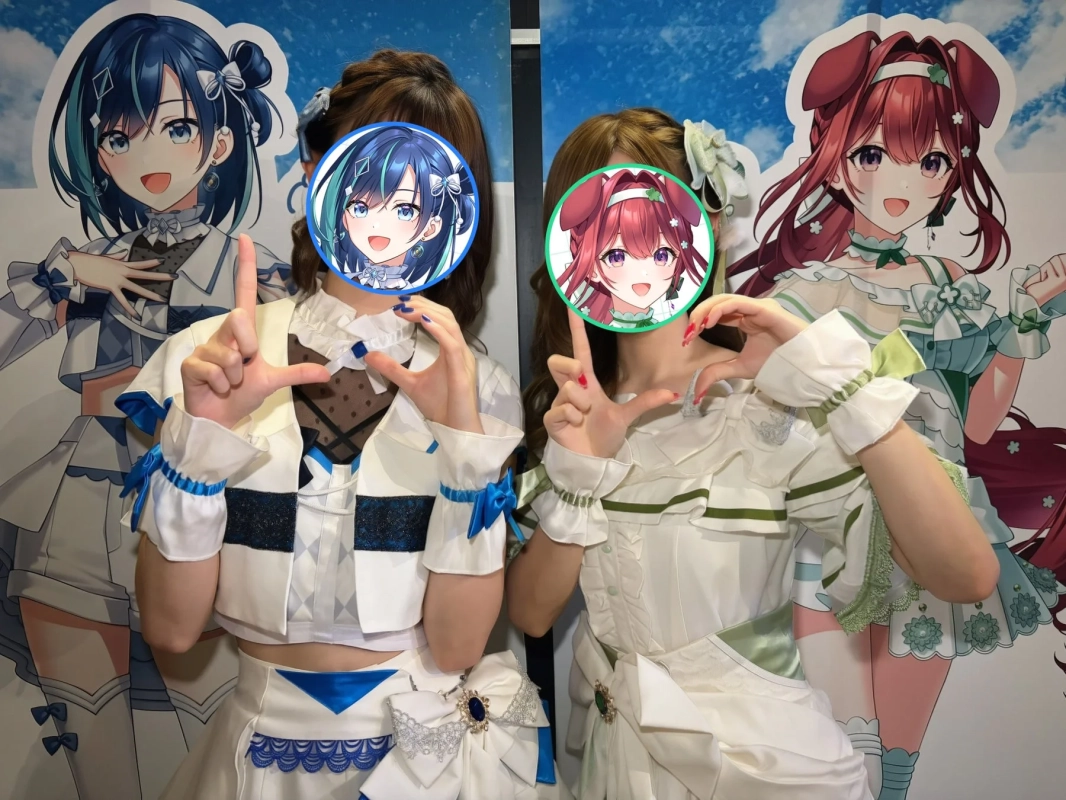2人の女性がアニメキャラクターの衣装を着てポーズをとっている。顔はキャラクターのイラストで隠されており、背景には同じキャラクターのパネルが飾られている。