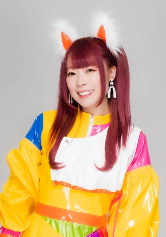 赤髪をツインテールにし、狐耳のカチューシャをつけた女性が、カラフルで光沢のある衣装を着て笑顔でポーズをとっているポートレート写真