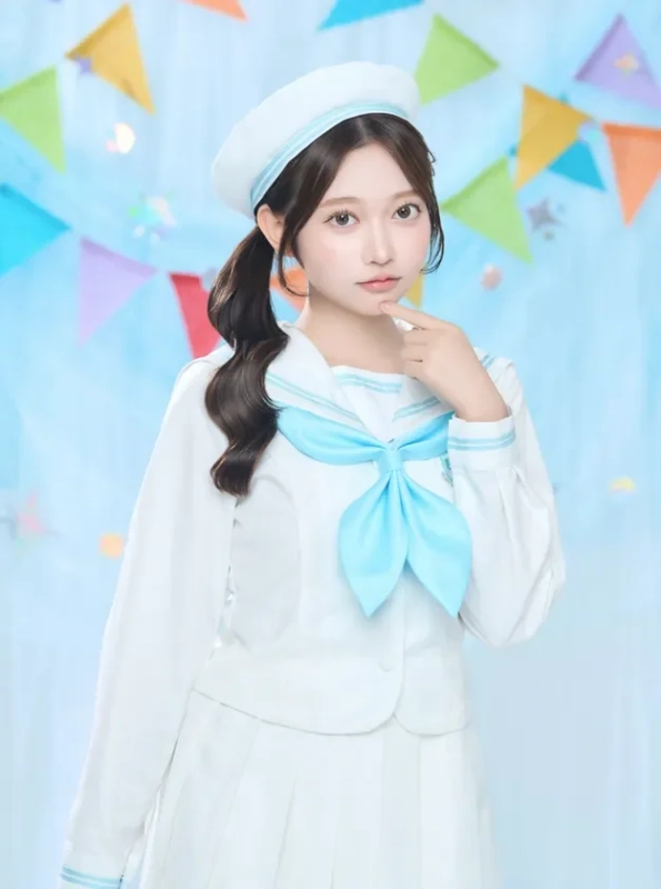 白いセーラー服とベレー帽を着用した若い女性が、明るい背景の前でポーズをとっています。青い大きなリボンが特徴的で、可愛らしい印象を与えています。