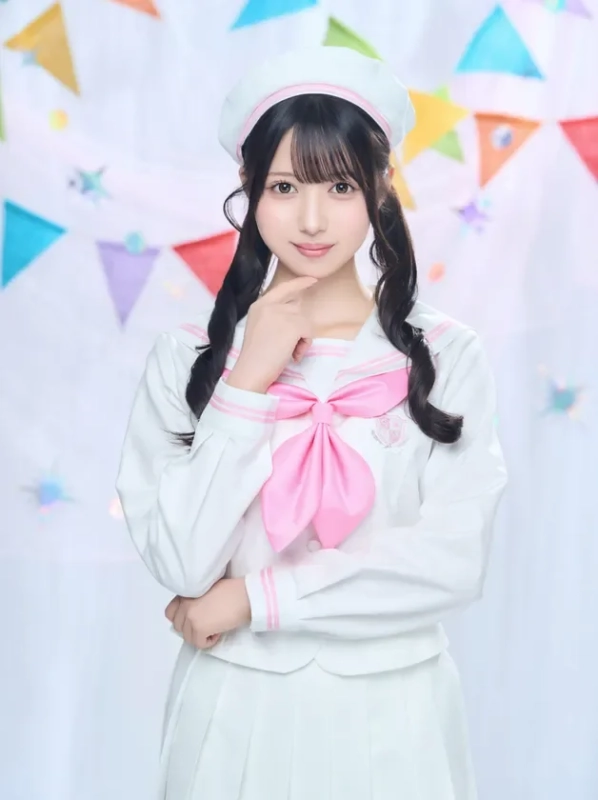ピンクのリボンと白いセーラー服を着た若い女性が、ベレー帽とツインテールで可愛らしいポーズをとっています。背景にはカラフルなガーランドが飾られ、明るく華やかな雰囲気のポートレートです。